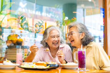 Happy Asian senior woman travel and shopping in the city on summer holiday vacation. Group of Healthy elderly women friends enjoy outdoor lifestyle having lunch eating food together at restaurant.