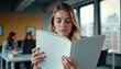 © Pete - Woman sits in office reading a blank magazine. Colleagues work at desks in background. Interior shot of a modern office space. Focused on woman reading. Business environment.