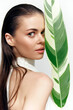© VICHIZH - Ethereal woman with long hair hiding behind a large tropical leaf, showcasing natural beauty and elegance in a white outfit, emphasizing skin texture and expression.