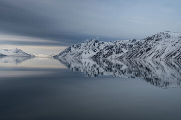 svalbard, norway. landscape reflection of mountains, snow and bay.