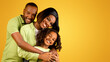 © Prostock-studio - Portrait of happy black family of three with cute daughter, joyful african american parents and their female child embracing and smiling together to camera, posing over yellow background
