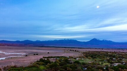 a serene twilight scene of flat desert plains, scattered greenery, and distant volcanic peaks, illum