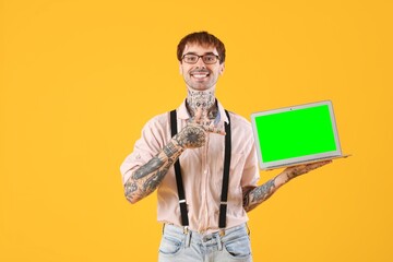 Canvas Print - Happy young man pointing at green screen of modern laptop on yellow background. Mockup for design