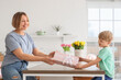 © Pixel-Shot - Happy mother receiving gift from her little son in kitchen. International Women's Day