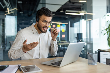 Sticker - Angry and irritated man with headset talking using laptop for video call. Businessman unhappy at online conference meeting.