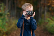 © Cavan Images - Young boy holding a vintage camera in a forest during autumn.