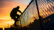 © Prasanth - Intruder's silhouette scaling a chain-link fence at dusk by industrial buildings, evoking tension and intrigue