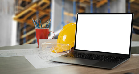 Poster - A laptop is open on a desk with a yellow hard hat and a red cup of pens. working table architect designer