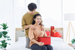 © Bangkok Click Studio - Portrait of young lovely sweet romantic asian happy couple love hugging embracing holding gift box presenting for Valentine's day sitting on the bed in bedroom at home smiling enjoy good time together