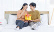 © Bangkok Click Studio - Portrait of young lovely sweet attractive asian happy couple love man giving surprise present gift box to beloved woman for Valentine's day in bedroom at home smiling enjoy good time romantic together