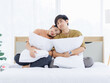 © Bangkok Click Studio - Portrait of young lovely sweet attractive asian happy couple love posing to camera smiling hugging pillow sitting on white bed in bedroom at home good time romantic together Valentine's day concept.