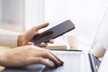 Poster - Woman expertly using a cutting-edge smartphone at her workspace, laptop on standby against the vague backdrop of a thriving office