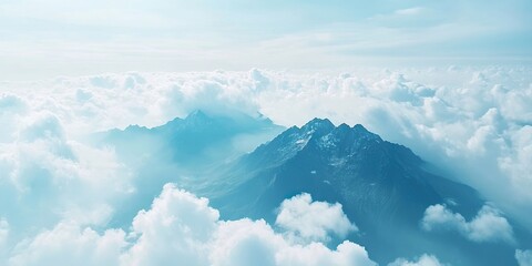 Wall Mural - Aerial view of majestic mountain peaks partially obscured by soft white clouds against a serene blue sky creating a tranquil picturesque landscape