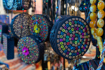 A collection of colorful purses and necklaces hang from a rack. The purses are made of different materials and have various designs, while the necklaces are made of beads and have different shapes