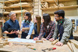 © Robert Kneschke - Young apprentices and mentor discussing woodworking project in lumberyard