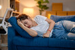 © Wasana - A woman is laying on a blue couch, looking sad and tired