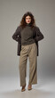 © Lustre Art Group  - Full length photo of young attractive woman, with brunette curly hairstyle, dressed formal attire posing against minimalistic grey setting. Concept of human emotions, self-expression, fashion, style.