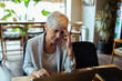© Davor - Stressed senior businesswoman working on laptop in modern cafe
