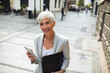© Davor - Senior professional businesswoman using smartphone downtown