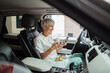 © Davor - Senior nurse eating salad on break in car and using smartphone