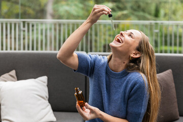 Woman taking cbd oil with a dropper smiling at home