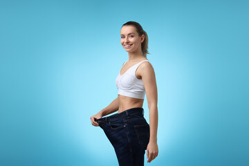 Wall Mural - Weight loss. Happy woman wearing big jeans on light blue background