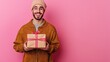 © vefimov - Happy man with beard wearing yellow coat, holding gift bag. Pink background.