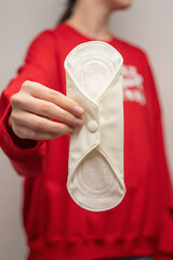 Wall Mural - A teenage girl in a red shirt with a reusable sanitary pad in her hands, close-up