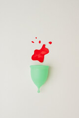 Wall Mural - Green menstrual cup with red drops on white background. Minimal concept.