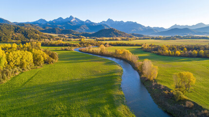 Wall Mural - Aerial view of winding river surrounded by lush green fields and mountains. landscape showcases vibrant autumn colors and clear skies