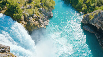 Poster - Aerial view of stunning waterfall cascading into turquoise river surrounded by lush greenery, creating serene natural landscape