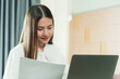 © Ekkasit A Siam - Asian female office worker reviewing documents at home, maintaining focus and determination while working remotely in a comfortable and relaxed atmosphere.
