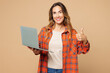 © ViDi Studio - Young smiling happy IT woman she wear orange shirt casual clothes hold use work on laptop pc computer show thumb up isolated on plain pastel light beige background studio portrait. Lifestyle concept.