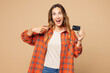 © ViDi Studio - Young shocked surprised woman she wear orange shirt casual clothes hold in hand point finger on mock up of credit bank card isolated on plain pastel light beige background studio. Lifestyle concept.