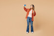 © ViDi Studio - Full body young woman she wear orange shirt casual clothes doing selfie shot on mobile cell phone post photo on social network show v-sign isolated on plain pastel beige background. Lifestyle concept.