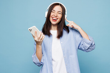 Wall Mural - Young happy Caucasian woman she wears shirt casual clothes listen to music in headphones use mobile cell phone isolated on plain pastel light blue cyan background studio portrait. Lifestyle concept.