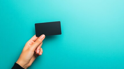 Poster - Woman hand holding a blank black card on a turquoise background, perfect for adding custom text or designs, ideal for marketing and advertising campaigns