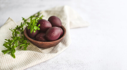 Wall Mural - Easter burgundy eggs in a clay plate on a white napkin, decorated with green willow branches on a light background, soft selective focus, copy space. Festive background with Easter symbols