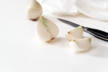 A white onion cut into quarters. A knife lies nearby