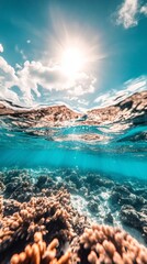 Poster - Half underwater shot showing a coral reef with sunlight filtering through the water surface and white clouds and blue sky in the background