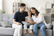 © fizkes - Family with preschooler daughter enjoy talk, light-hearted funny conversation seated on sofa. Parents and kid girl relaxing together in living room, feel untroubled, looks carefree on leisure at home
