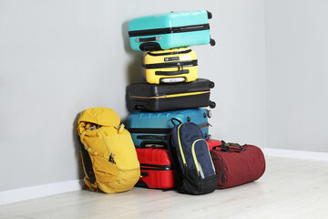 Wall Mural - Stack of colorful suitcases, backpacks and bag on floor near light wall