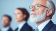 © Sergey - An image of diverse businesspersons from different generations, primarily focusing on an older man with a thoughtful expression. The background is blurred.