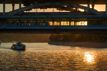 Sightseeing boat under the bridge at sunset