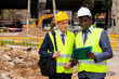 © JackF - Two engineers, Caucasian and African-american men in hardhats and warnvests, standing and talking about road paving works documentation.