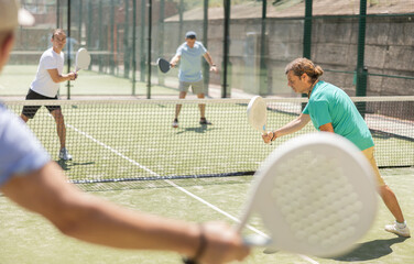 Wall Mural - Adult man and elderly man doubles playing against two men in padel tennis on court