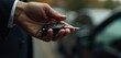 © Makaron - A close-up of a hand holding a car key fob, symbolizing car ownership, leasing, or the start of a journey in a modern urban setting.