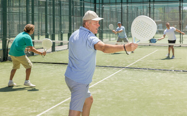 Mature sporty man playing padel game in court on sunny day