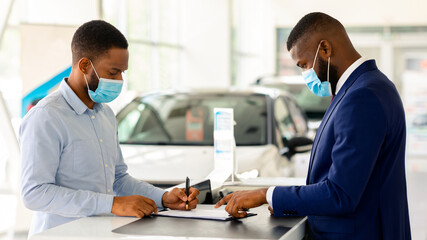 Wall Mural - Black Man In Medical Mask Buying New Car In Dealership Office During Coronavirus Pandemic, African American Male Customer Signing Papers With Salesman In Modern Automobile Showroom, Free Space