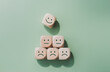 © LAONG - World mental health day concept or feedback rating and positive customer review, wood cube stacking with emotion face icon on pastel green background